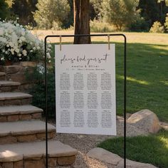 a sign that is sitting in the grass next to some steps and flowers on top of it