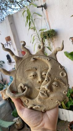 a person holding up a clay sculpture with faces on it