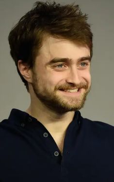 a close up of a person wearing a blue shirt and looking at the camera with a smile on his face