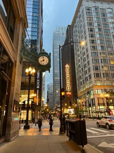 a clock on the side of a street in front of tall buildings with lights at night