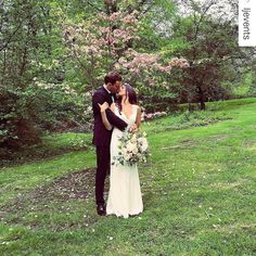 a bride and groom standing in front of a blooming tree with their arms around each other