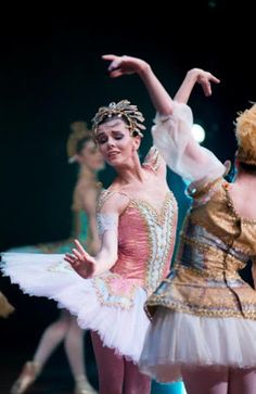 two ballerinas in tutu and leotards on stage with one holding her arm out