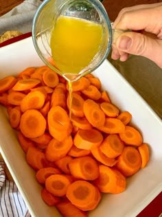 someone pouring orange juice into a bowl of sliced carrots