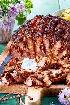 a large piece of meat sitting on top of a cutting board next to some flowers