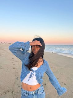 a woman standing on top of a sandy beach next to the ocean with her hands behind her head