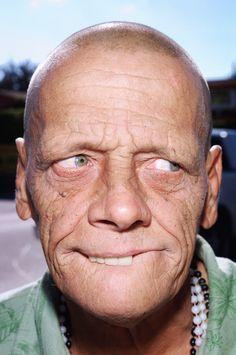 an old man with a green shirt and beaded necklace on his neck looking at the camera