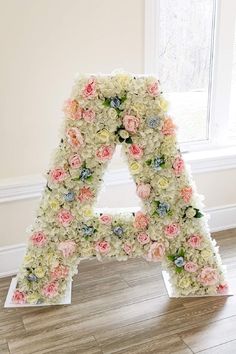 the letter is made out of flowers and sits on top of a wooden floor in front of a window