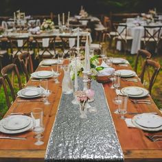 a long table with silver sequins and white plates on it is set for an outdoor dinner