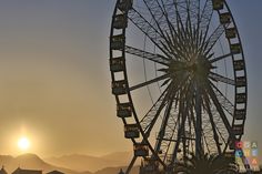 a ferris wheel sitting in the middle of a field with mountains in the background at sunset