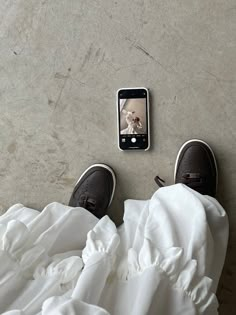 someone's feet on the ground with their cell phone and white sheets covering them