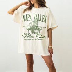 a woman wearing a napa valley wine club t - shirt and short shorts is standing in front of a white wall