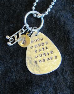 a silver necklace with a guitar pick and the words when words fail music speaks on it