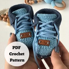 someone is holding up a crocheted blue boot with brown leather tags on it