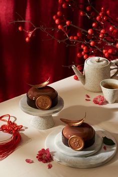 three desserts on plates with red flowers and teapots in the back ground