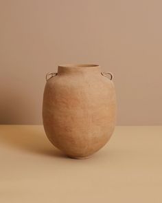 a brown vase sitting on top of a table next to a beige wall and floor