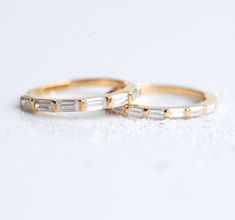 two gold wedding bands with baguettes on them sitting on a white table top