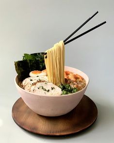 a bowl filled with noodles and vegetables on top of a wooden plate