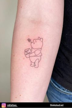 a small tattoo on the arm of a person with a bear holding a sign that says,