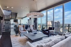 a living room filled with lots of furniture and tall windows next to a stair case