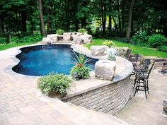 a backyard with a swimming pool surrounded by rocks and landscaping items, including chairs and tables