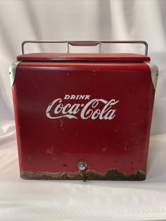 an old coca - cola cooler sitting on top of a white sheet