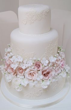 a white wedding cake with pink flowers and lace