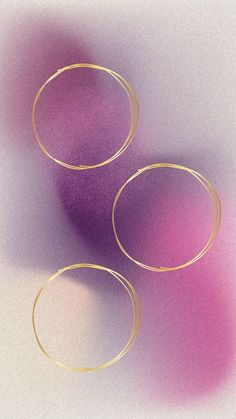 three gold rings on a white surface with pink and purple light coming from the top