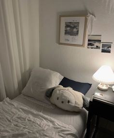 a white teddy bear sitting on top of a bed next to a night stand and lamp