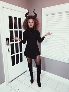 a woman dressed as a demon poses in front of a door with horns on her head