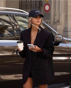 a woman is walking down the street while holding a coffee cup and cell phone in her hand