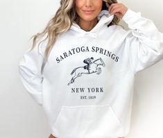 Saratoga Springs Horse Racing Sweatshirt, New York Race Track Hoodie Super soft and comfy fleece hoodie made especially for cool nights. * 50% cotton, 50% polyester * Medium-heavy fabric (8.0 oz/yd² (271.25 g/m * Double-lined hood * Double-needle stitching throughout * Air-jet spun yarn with a soft feel and reduced pilling * 1x1 athletic rib knit cuffs and waistband with spandex * Front pouch pocket PROPER SIZING Please see photos to see a specific sizing chart for this sweatshirt style. These s Spring Sports Hoodie With Letter Print, Cozy Crew Neck Sports Hoodie, Spring Sports Sweatshirt With Kangaroo Pocket, Cozy Fit Sweatshirt For Sports In Spring, Sporty Pre-shrunk Long Sleeve Hoodie, Sporty Cotton Hoodie With Comfortable Fit, Comfortable Cotton Sporty Hoodie, Cozy Sports Hoodie For Spring, Cozy Hoodie For Spring Sports