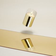 a candle that is floating in the air next to some gold colored objects on a table