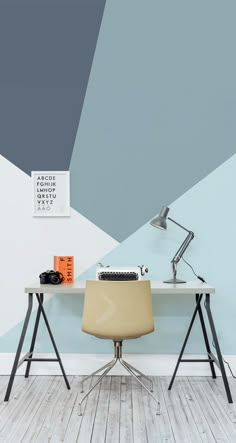 a desk with a chair and a lamp on it in front of a blue wall