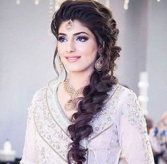 a woman with long dark hair wearing a white dress and gold jewelry is posing for the camera