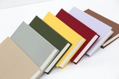 five different colored books lined up on a white table top with one open book in the middle