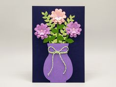 a purple vase filled with flowers on top of a blue card