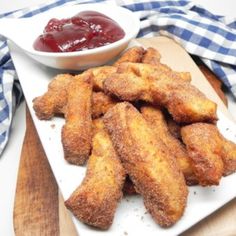 fried chicken sticks with ketchup on a white plate next to a bowl of ketchup