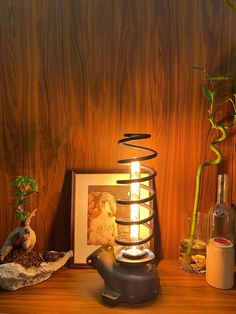 a table topped with a vase filled with plants and a lit candle next to it