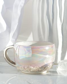 a white cup sitting on top of a table next to a window covered in curtains