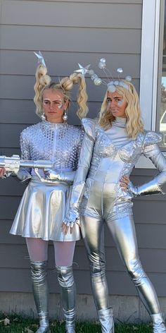 two women dressed in silver standing next to each other on the grass near a house