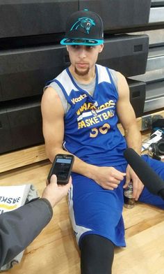 a basketball player sitting on the floor with two cell phones in his hand and another person holding a camera