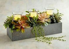 some candles are sitting in a box with succulents and flowers on it