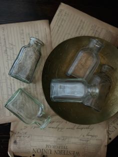 three glass jars sitting on top of an open book next to some empty glasses and papers