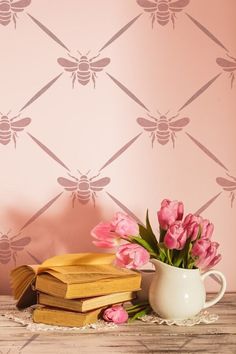 pink tulips are in a vase next to books and a bee wallpaper