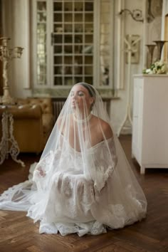 a woman in a wedding dress sitting on the floor with her veil over her face