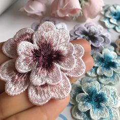 a hand is holding several small flowers in different colors and sizes, including pink, blue, gray, and white