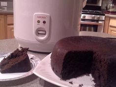 a chocolate cake sitting on top of a white plate next to an electric rice cooker