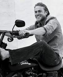 a man sitting on top of a motorcycle with his hand in the air and smiling