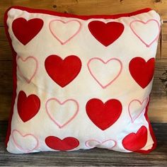 a red and white pillow with heart shapes on it, sitting on a wooden surface