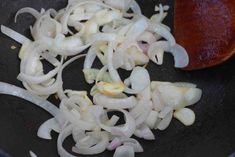 onions being sauteed in a frying pan with a wooden spoon on the side